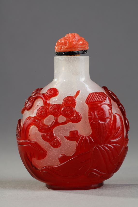 Snuff bottle  red overlay glass with Shou Lao holding a peche of longevity and looking at peches and on the other side of a character holding a cup on a tray in front of a pine - China 1800/1850 | MasterArt
